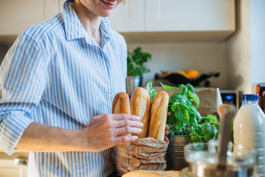 A midsection of young woman standing indoors in kitchen, unpacking shopping bag.